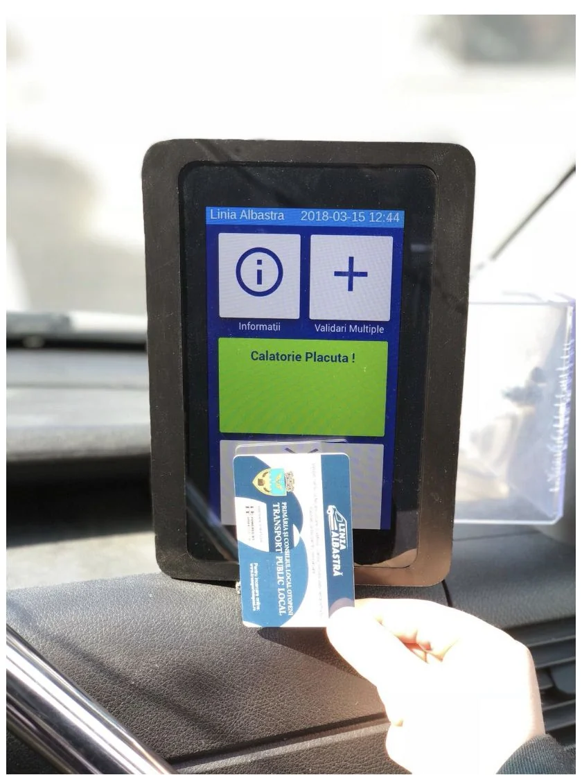 Aparatul de taxat montat pe bordul vehiculului, cu ecran tactil și un card Linia Albastră prezentat în dreptul cititorului