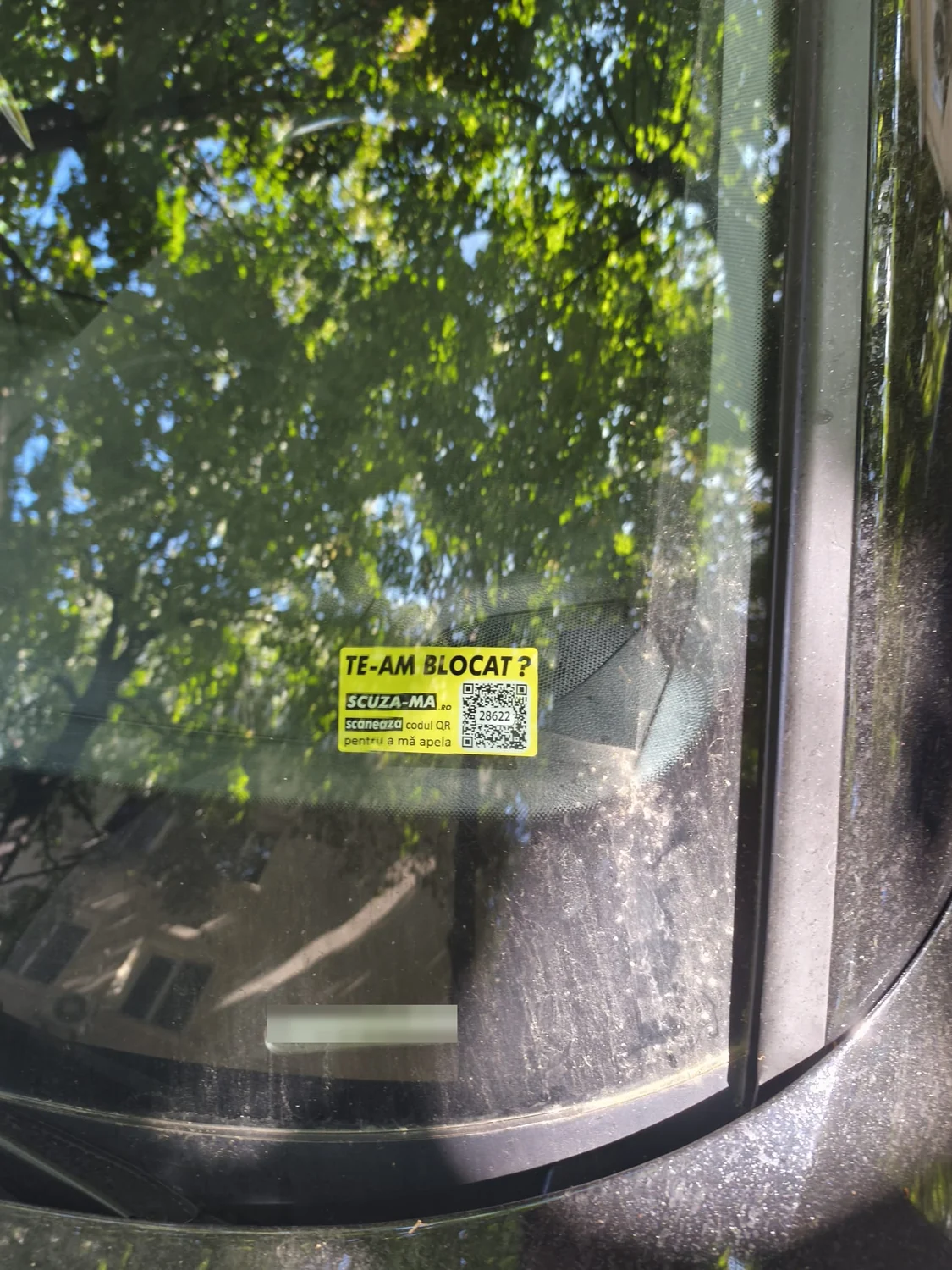 Stickerul galben Scuza-Ma.ro aplicat pe parbriz, cu textul „Te-am blocat?”, codul QR și codul numeric